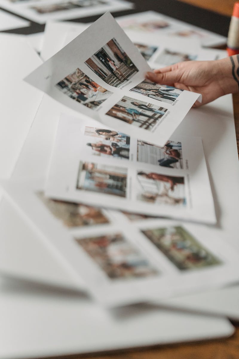 Crop anonymous person looking through printed photos scattered on floor in light room